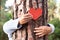 A senior adult woman in the woods hugging a tree with her arms. With her fingers she tells us that every tree has a heart. Earth