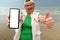 Senior adventure is ageless woman with a mobile phone with white blank for your ads on the sea beach near old center of Antalya.