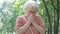 Senior allergic woman sneezing in summer or spring park with pollen flying around. Female Caucasian retiree having