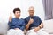 Senior Asian couple looking at camera and giving thumbs up while sitting on sofa at home.