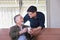 Senior Asian man holding a cup of coffee from his son who came to visit him with both smiling on their face