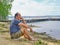 Senior asian man sitting on the sandy beach near the lake and pondering something