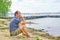 Senior asian man sitting on the sandy beach near the lake and pondering something