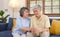 Senior asian woman comforting her husband from depressed emotion while sitting on sofa at home living room, old retirement