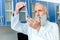 Senior bearded chemist in white coat holding tube with reagent in chemical laboratory