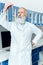 Senior bearded scientist in white coat looking at tube with reagent in chemical laboratory