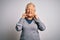 Senior beautiful grey-haired woman wearing golden queen crown over white background covering ears with fingers with annoyed