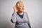 Senior beautiful grey-haired woman wearing golden queen crown over white background smiling with hand over ear listening an