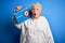 Senior beautiful woman holding vintage radio standing over isolated blue background scared in shock with a surprise face, afraid