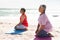 Senior biracial couple practicing kneeling yoga pose while meditating on exercise mat at beach