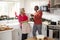 Senior black couple opening champagne and laughing together in the kitchen while preparing dinner on Christmas Day, selective focu