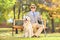 Senior blind gentleman sitting on a bench with his dog, in a par