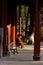 Senior Buddhist monk sits on a bench in front of a vibrant red building.