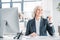 Senior businesswoman in formal wear sitting at workplace and triumphing