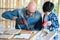 A senior carpenter and boy wearing goggle in the modern wood workplace. A man teach kid how to use screwdriver. Young child