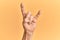 Senior caucasian hand over yellow isolated background gesturing rock and roll symbol, showing obscene horns gesture