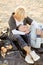 Senior caucasian husband lying on wife knees and plaid, champagne and fruits on sand beach.