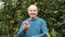 The senior caucasian man in blue sweater enjoys the crop of apples in the garden