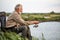 Senior caucasian man fishing outside in evening on lake in summer sitting on chair