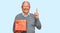 Senior caucasian man holding gift surprised with an idea or question pointing finger with happy face, number one