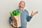 Senior caucasian man holding paper bag with bread and groceries celebrating achievement with happy smile and winner expression