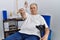Senior caucasian man at physiotherapy clinic holding crutches pointing to you and the camera with fingers, smiling positive and