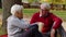 Senior Caucasian married couple sit on the ground and talk drink coffee in the park medium shot selective focus happy