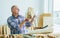 Senior Caucasian retired old male woodworker, carpenter reading, rechecking and comparing drawing plan with finish wooden figure