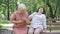 Senior Caucasian woman walking friend with heart attack to bench in summer park. Worried female retiree calling