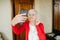 Senior, colorfully dressed woman is taking pictures of her beauty at home