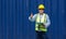 Senior contractor in safety vest and yellow hardhat holding document clipboard, stand with finger thumbs up in front of a large