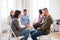 Senior counselor with clipboard talking to a man during group therapy.