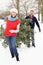 Senior Couple Carrying Christmas Tree In Snow