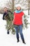 Senior Couple Carrying Christmas Tree In Snow