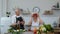 Senior couple cooking salad with vegetables. Woman dancing holding fresh slices of pepper on eyes