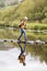 Senior Couple Crossing River Whilst Hiking In UK Lake District