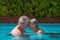 Senior couple floating in the swimming pool water head to head, happy retirees enjoying summer vacation
