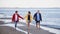 Senior couple holding hands with their preteen granddaughter and walking on sandy beach.