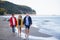 Senior couple holding hands with their preteen granddaughter and walking on sandy beach.