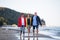 Senior couple holding hands with their preteen granddaughter and walking on sandy beach.