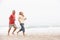 Senior Couple On Holiday Running Along Beach