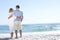 Senior Couple On Holiday Walking Along Sandy Beach Looking Out To Sea