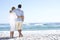 Senior Couple On Holiday Walking Along Sandy Beach Looking Out To Sea