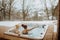Senior couple in kintted cap enjoying together outdoor bathtub and view at their terrace during cold winter day.