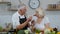 Senior couple in kitchen. Grandmother and grandfather feeding each other with raw vegetable salad