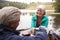 Senior couple by a lake, man pouring coffee to his wifeï¿½s cup, over shoulder view, Lake District, UK