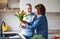 A senior couple in love indoors at home, putting flowers in vase.