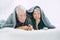 Senior couple lying on front and gesturing finger on lips on bed. Elderly couple spending leisure with each other. Happy old