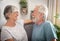 A senior couple relax on the armchair and laugh looking each other.  Man with beard and white hair. Bright light from the window