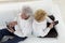 Senior Couple seated back to back playing with tablets and iphones